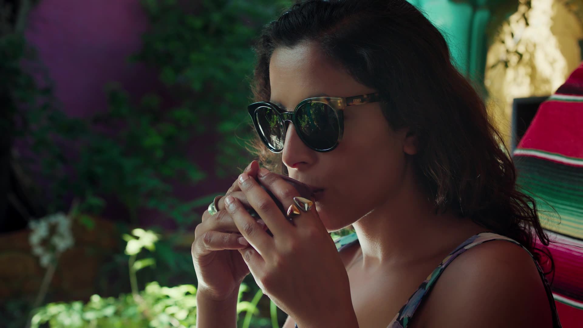 Amira Chebli in sunglasses, drinking from a cup, in Perception